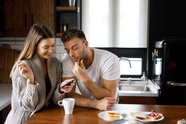 istock Young affectionate couple looking at mobile phone in the kitchen 1201663719