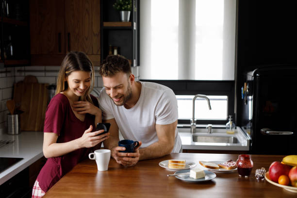 istock Young affectionate couple looking at mobile phone in the kitchen 1201663977