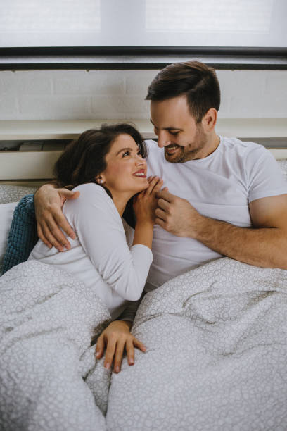 istock Happy young couple embracing and looking at each other while lying in bed together 1201665179