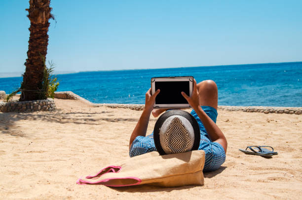 전자 리더와 함께 해변에서 읽는 젊은 남자 - electronic book reader 뉴스 사진 이미지