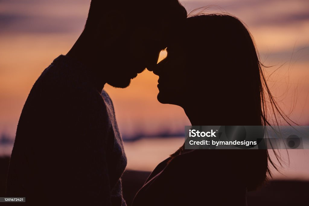 Silueta de pareja joven teniendo momentos románticos contra el fondo de la puesta de sol - Foto de stock de Parejas libre de derechos