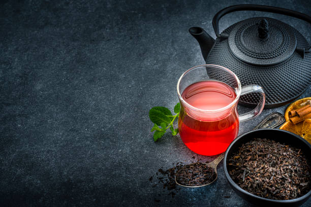 Herbal tea. High angle view of a black tea cup, teapot and a bowl filled with dried black tea shot on dark black background. The composition is at the right of an horizontal frame leaving useful copy space for text and/or logo at the left. Predominant colors are black and red. High resolution 42Mp studio digital capture taken with Sony A7rii and Sony FE 90mm f2.8 macro G OSS lens