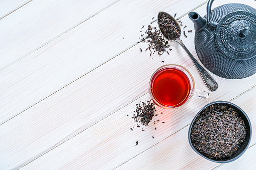 Herbal tea. Top view of a black tea cup, teapot and a bowl filled with dried black tea leaves shot on white table. The composition is at the right of an horizontal frame leaving useful copy space for text and/or logo at the left. Predominant colors are white and red. High resolution 42Mp studio digital capture taken with SONY A7rII and Zeiss Batis 40mm F2.0 CF lens