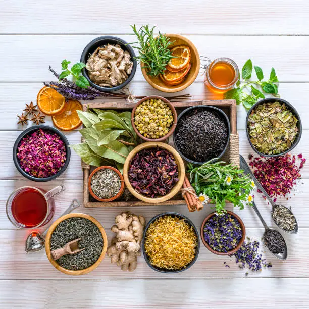 Herbal tea. Large variety of dried herbs and flowers for preparing healthy detox infusions shot from above on white table. The composition includes dried part of plants like hibiscus, calendula, rose petals, chamomile, green tea, bay leaves, cinnamon sticks, ginger, lemons, mint leaves, a honey jar and dried orange slices among others. High resolution 42Mp studio digital capture taken with Sony A7rii and Zeiss Batis 40mm F2.0 CF lens