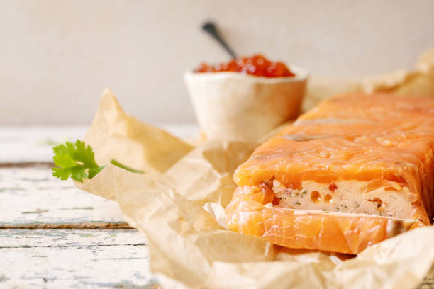 Red salmon caviar in ceramic bowl and homemade salmon terrine served with butter on crumpled paper over old wooden table. Rustic style