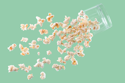 Delicious looking fresh popcorn falling from a suspended glass on a light background. Fast food and fun concept.