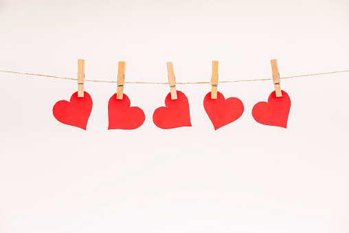 Clothes pegs and red paper hearts on rope isolated on white background. Valentines day concept