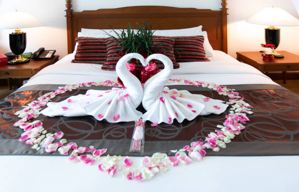 ロマンチックなベッドルームインテリア、キススワン折り紙タオルと新婚カップルのためのベッドの上に新鮮なピンクの白いバラの花びらの装飾を振りかけた。結婚式, 記念日, ハネムーン, � - honeymoon romance wedding bedroom ストックフォトと画像