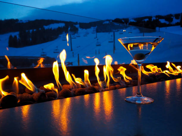 Apres Ski with a fire and a drink, in front of the slopes Relaxing in the evening after skiing with a martini in front of a fire table, with a view of the slopes apres ski stock pictures, royalty-free photos & images
