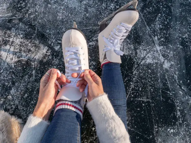 Photo of Young woman on frozen lake putting on ice skates at sunset getting ready to have fun and enjoy winter vacations