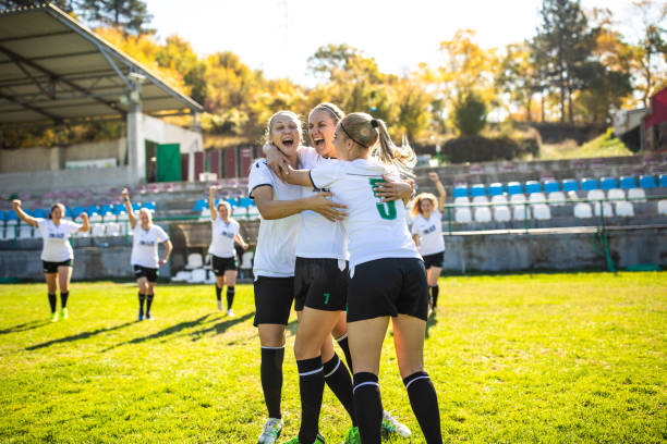 Excited female soccer team celebrating goal on the field Young female soccer team celebrating goal, smiling and embracing on soccer field during sunny summer day soccer team stock pictures, royalty-free photos & images