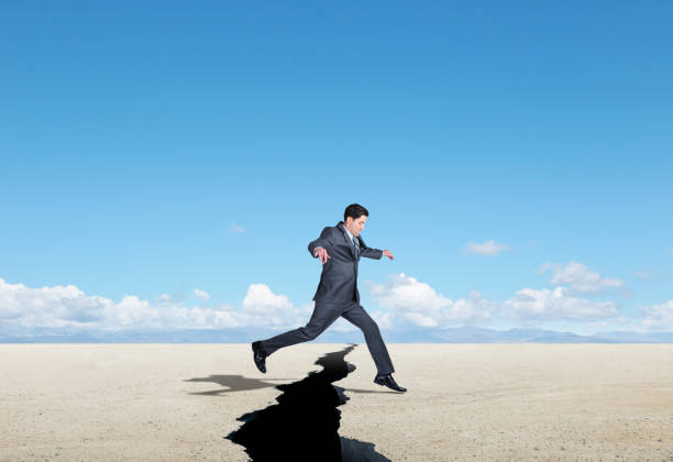 istock Businessman Jumping Over Large Crack In The Ground 1201688546