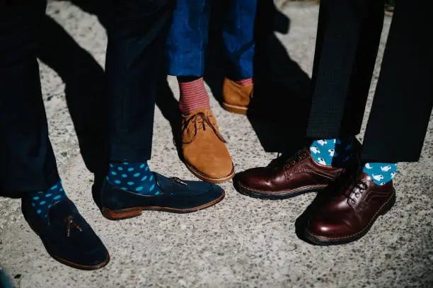 Photo of Groom's and groomsman feet with funny colorful socks. The men in stripy socks. Bright, vintage, brown shoes. Fashion, style, beauty.