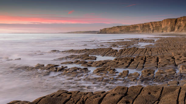 agua de mar, lavando sobre una orilla rocosa, mientras que el sol se pone en el horizonte. una larga exposición ha creado un mar lechoso - horizon over water england uk summer fotografías e imágenes de stock