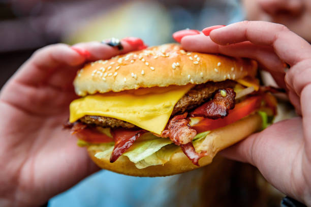 woman hand is holding a fresh burger before eating on street - bacon cheeseburger imagens e fotografias de stock