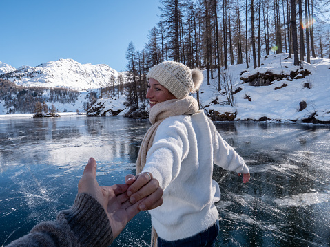 Follow me to concept; Happy young woman leading boyfriend to frozen lake at sunset ice skating