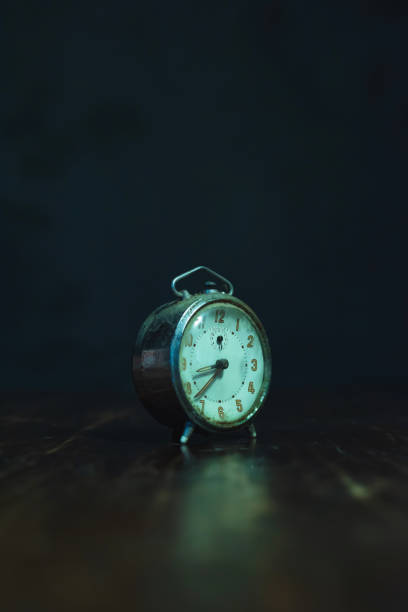 Dusty old alarm clock on worn wooden table.