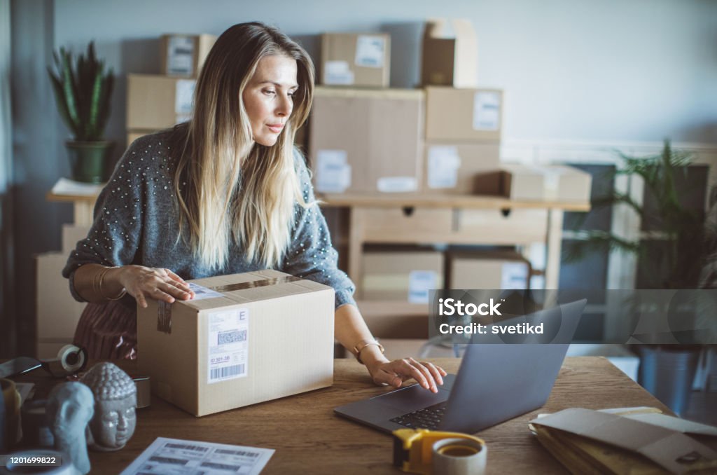 Help of technology in delivery business Working woman at online shop. She wearing casual clothing and checking on laptop address of customer and package information Internet Stock Photo