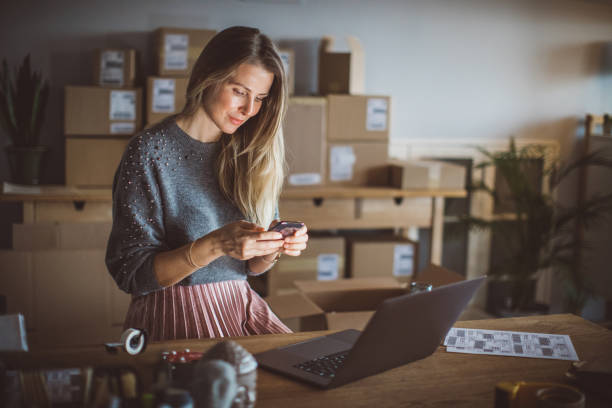 Organizing work in delivery business Working woman at online shop. She wearing casual clothing and using laptop and mobile phone for work organization cardboard box photos stock pictures, royalty-free photos & images