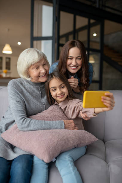 fille gaie prenant un selfie avec la grand-mère et la maman. - wireless technology cheerful granddaughter grandmother photos et images de collection