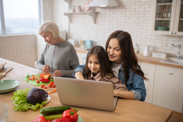 mama z córką na laptopie, babcia przygotowuje jedzenie w kuchni. - grandparent using computer laptop dining table zdjęcia i obrazy z banku zdjęć