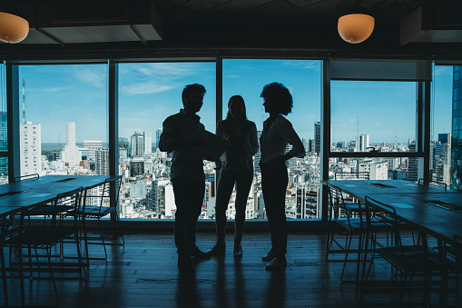 Silhouette of three business people in a modern office. Skyline of the city in the background. They are brainstorming together.