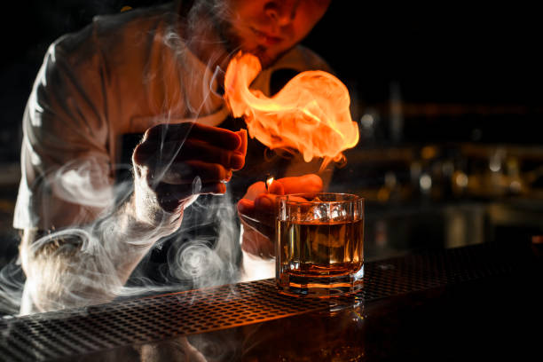 professional bartender serving the transparent alcoholic cocktail sprinkling with the lemon juice on the match making fire - drink on top of ice food imagens e fotografias de stock