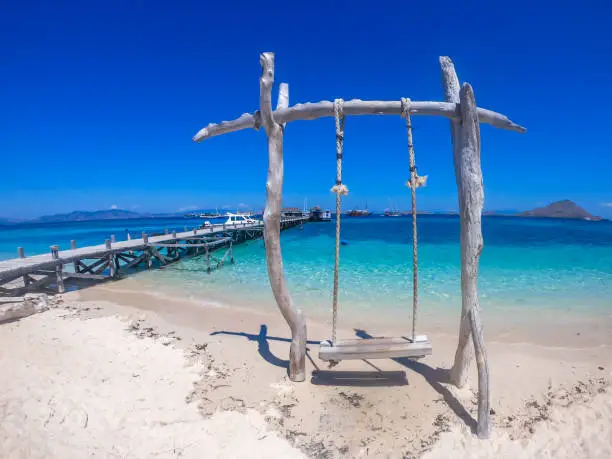 Wooden made swing located in a very shallow wateron a beach in Komodo National Park, Flores, Indonesia. There is a clear sea in front of it and some other islands in the back. Happiness and adventure