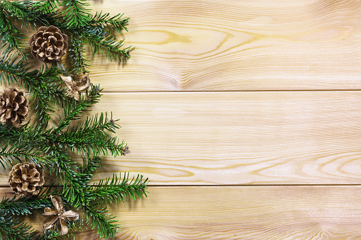 Green fir branches with pine cones on the edge of a textured wooden table. Space for text