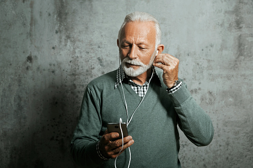 Senior man in sweater listening music with headphones