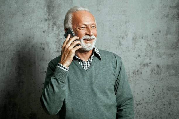 istock Senior man in sweater holding smart phone talking 1201724063