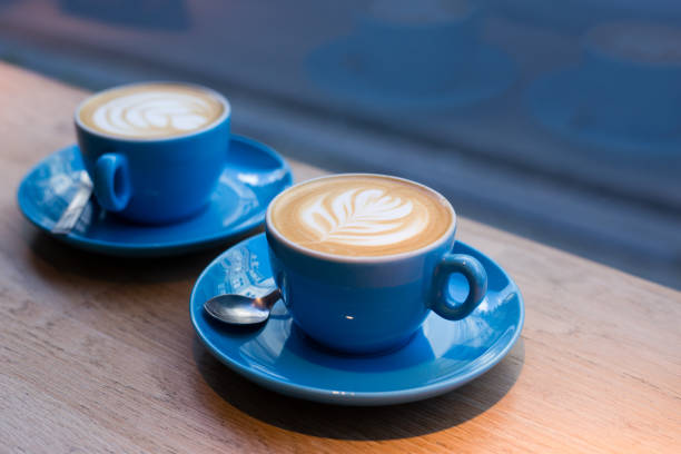 due tazze di cappuccino con arte del latte su tavolo in legno, tazza di ceramica blu al bar. cultura del caffè. - morning coffee coffee cup two objects foto e immagini stock