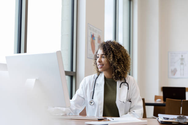 Mid adult female doctor reviews patient records on desktop PC The mid adult female doctor reviews her patient's records on her computer in her office. medical insurance data stock pictures, royalty-free photos & images