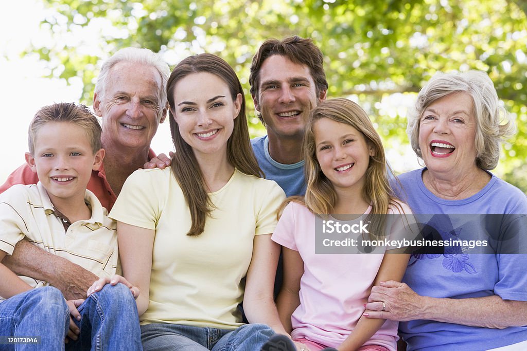 Three-generation family smiling at the park together Extended family sitting in park outdoors smiling 20-29 Years Stock Photo