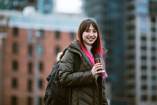 A young woman enjoys time in the city of Seattle, Washington.  She smiles for a portrait, holding a reusable coffee cup.