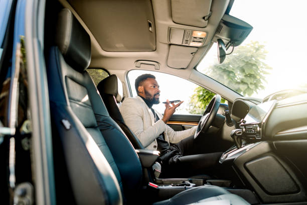 istock Young successful African American businessman talking on speakerphone through microphone with client, sitting in the expensive car. Negotiations and business meetings. 1201733314