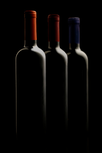 Bottles of red wine grouped with labels of different colors in the foreground on gray background