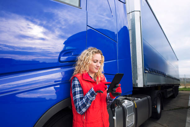 Professional truck driver setting up navigation for destination. Checking his route on tablet computer and standing by long vehicle. Transportation service.