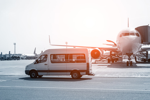White VIP service van running on airport taxiway with big passenger airplane on background. Business class service at airport. Security intelligence agency hurrying at airfield.