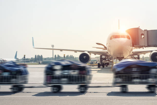 荷物の動きは、明るい晴れた日に空港で誘導路で現代の飛行機に乗客の荷物を高速で配達するトロリーカートをぼかしました。日没時または日の出時に背景に民間航空機 - luggage cart ストックフォトと画像