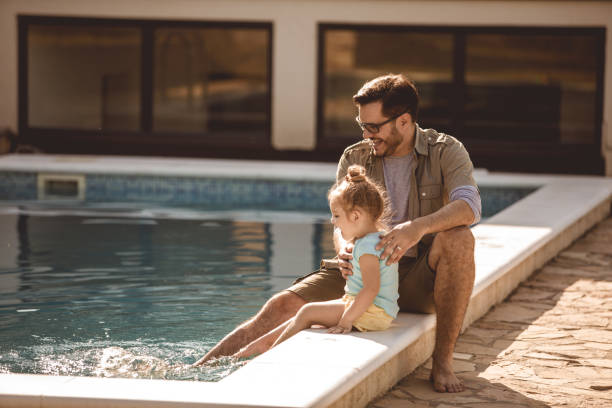 istock Toddler and her father having fun while splashing the water in swimming pool with their feet 1201756708