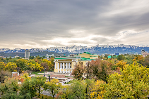 Cityscape of Almaty Kazakhstan with the landmark Abay National Opera House and the Ile Alatau Mountains in the background.