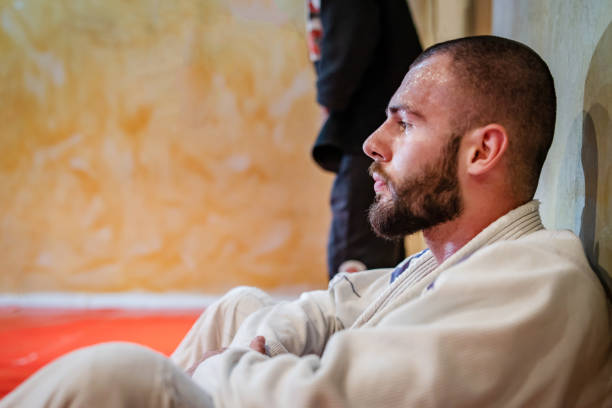 brasilianischejiu jitsu judo oder karate-kämpfer athlet sitzt auf dem tatami und eine bremse aus dem training ruhen müde - ju jitsu stock-fotos und bilder