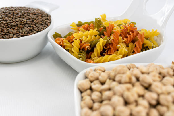 Close up view of colorful pasta, chickpeas and lentils in white bowls on white background