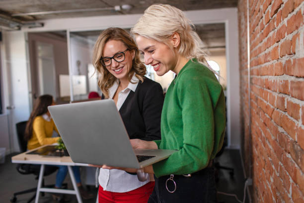 Success is the product of teamwork Two female colleagues working together on the laptop while standing travel agency stock pictures, royalty-free photos & images