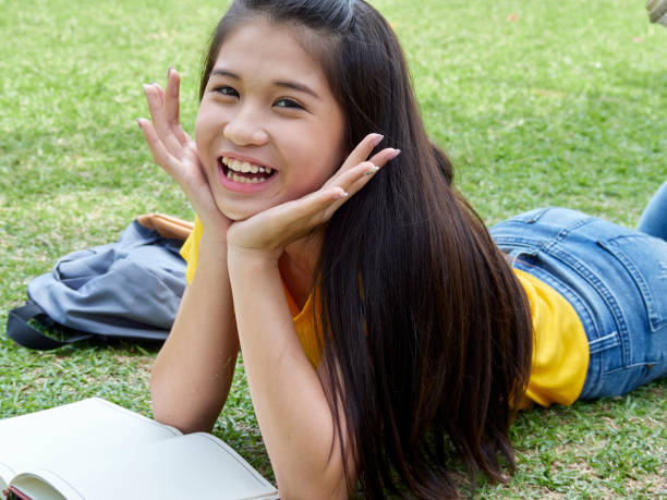 Young woman reading book in the park on the grass in sunny spring park. Student studying outdoors.