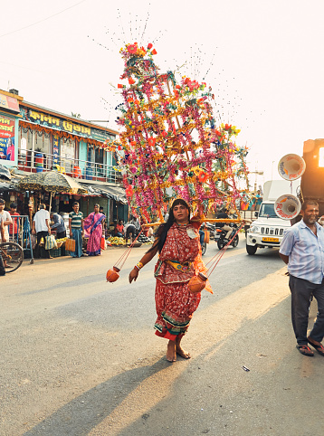 Colourful procession of Gajan festival in streets. A male performer, dressed as woman, dancing in the middle of a street, part of a large religious rally happening there. He is carrying large multicolor headgear, finely decorated with zari and foils. Pedestrian are enjoying his performance.
Gajan is a Hindu festival, dedicated to Lord Shiva, celebrated mostly in West Bengal. Photo taken at Ramnagar, Midnapore district, West Bengal on 04/19/2019 during evening hour.