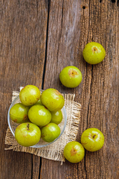 uva spina indiana fresca in ciotola di vetro su sfondo di legno - gooseberry foto e immagini stock