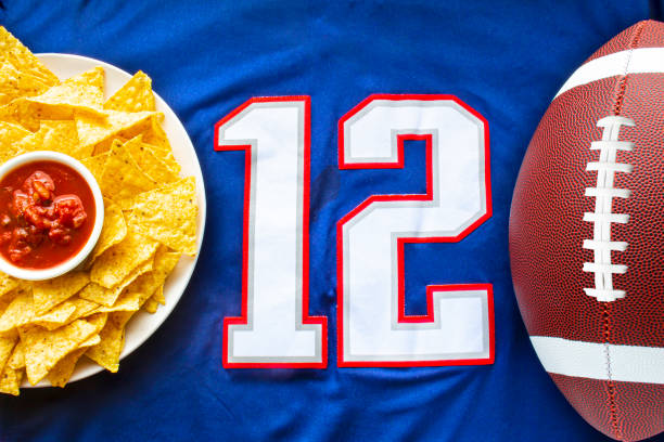 an american football with organic nacho chips and mild salsa on a white blue football jersey with the 12 number on horizontal view - american football football food snack imagens e fotografias de stock