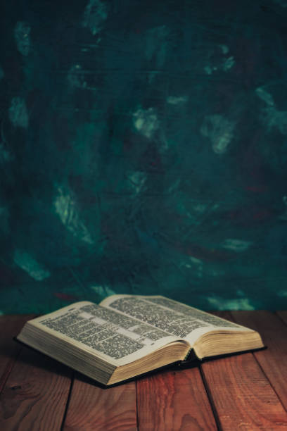 istock Open bible on a red wooden table. Beautiful green wall background. 1201798481